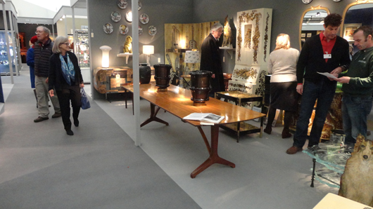The stand of Holly Johnson Antiques at the British Antique Dealers’ Fair in London, featuring a fine dining table dating from the early 1960s by the English Arts and Crafts-influenced designer Edward Barnsley (foreground), priced at £16,750 ($28,000). Image Auction Central News.